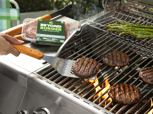 Beyond Burgers cooking on a gas grill alongside asparagus