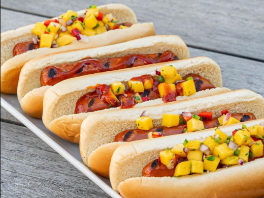 Five grilled Lightlife dogs on a tray topped with ketchup and fruit salsa